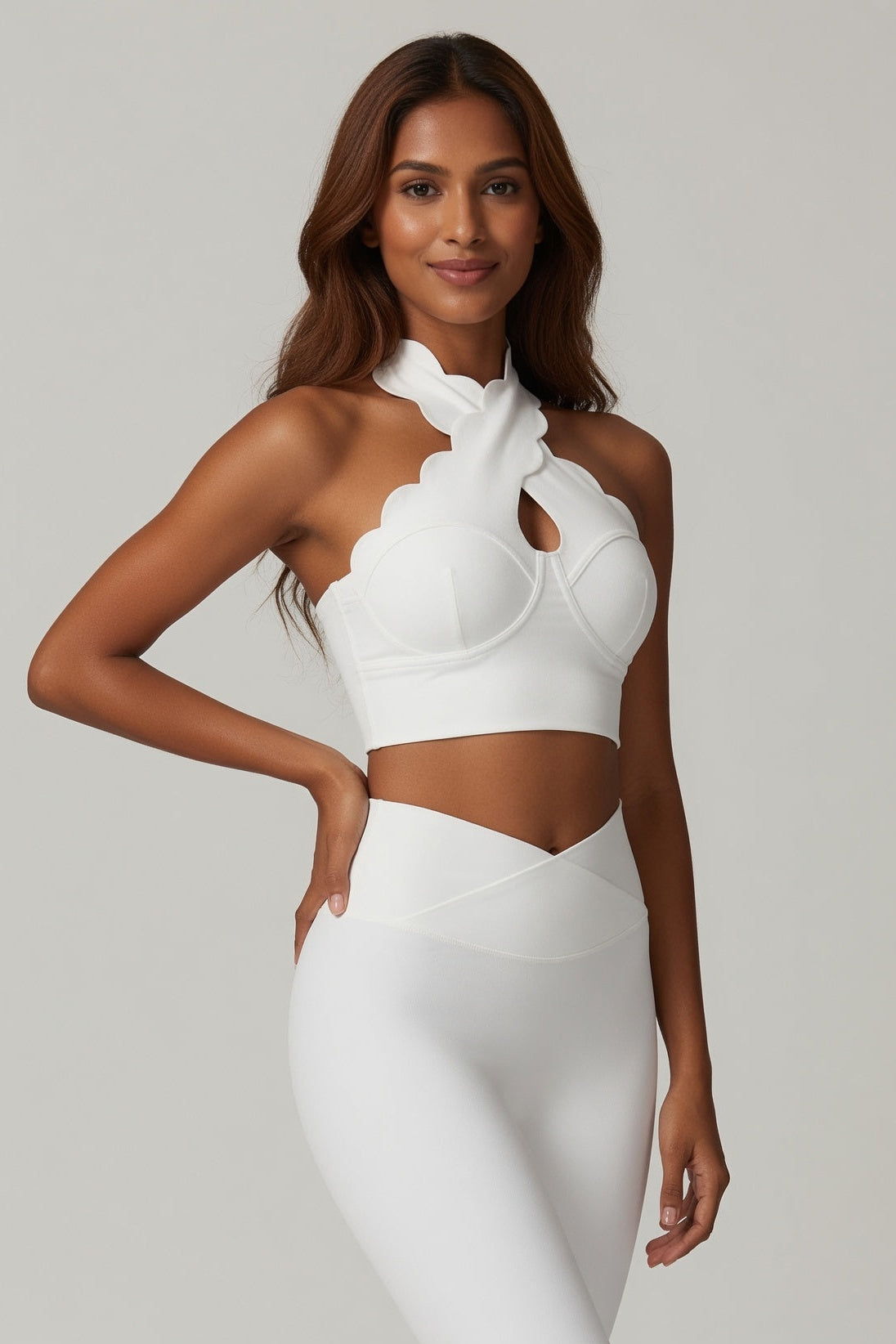 Woman wearing a white outfit with a scalloped neckline on a plain background